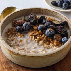 Sweet oatmeal topped with fresh blueberries and blackberries, served with milk in a rustic ceramic bowl.