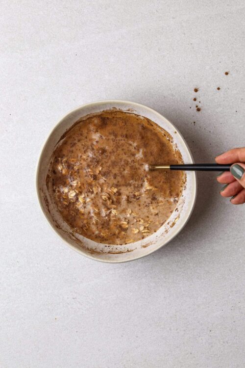 Creamy oatmeal with cinnamon and oats in a white bowl on a white surface.