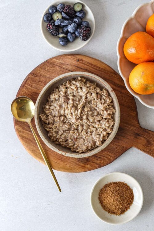 Creamy cooked oats in a bowl with fresh berries and oranges on a wooden serving board.