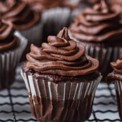 Rich chocolate cupcake with swirled frosting on cooling rack.
