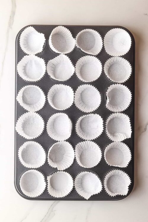 Light paper cupcake liners on a baking sheet ready for baking.