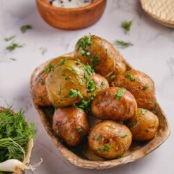 Buttered roasted baby potatoes with fresh herbs on rustic dish.