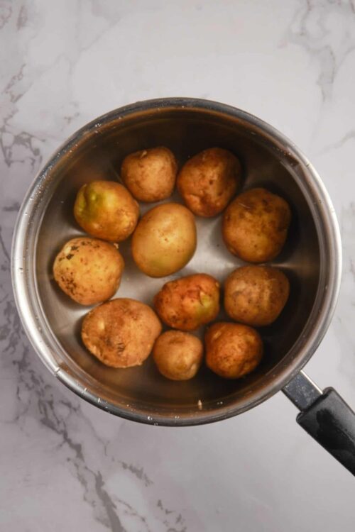 Small potatoes soaking in a stainless steel pot with water.