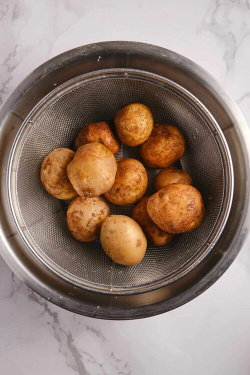 Baked potatoes in a stainless steel colander ready for cooking.