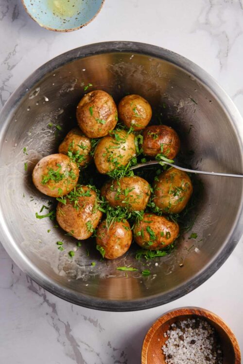 Fresh roasted potatoes garnished with chopped herbs in a stainless steel bowl.