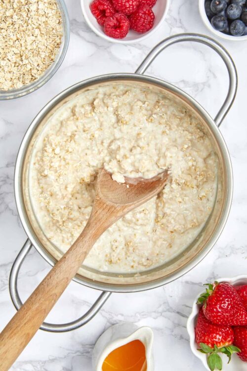 Creamy oatmeal with fresh berries and breakfast toppings on white marble surface.