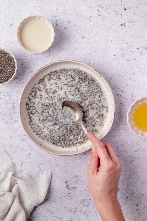 Black chia seeds soaking in milk on a white plate.