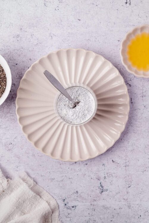Rich chia seed pudding in a glass on a textured surface with breakfast ingredients.