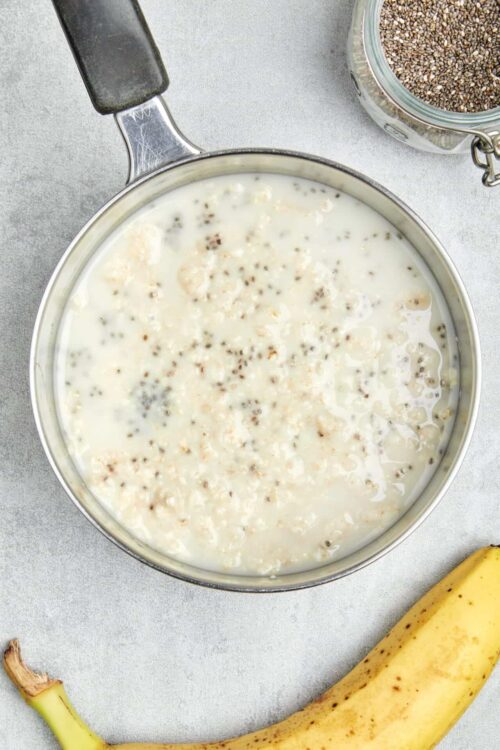 Creamy chia seed pudding in a saucepan with banana and chia seeds nearby.