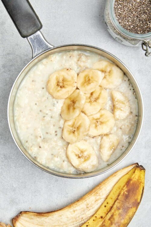Creamy banana and chia seed pudding in a saucepan with fresh banana slices on top and a banana peel nearby.