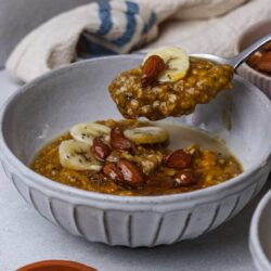 Creamy banana oatmeal topped with almonds and chia seeds in a ceramic bowl.
