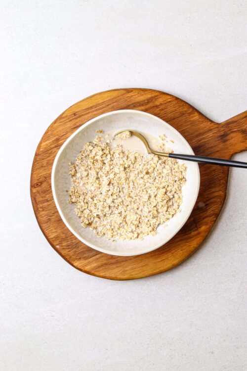 Creamy rolled oats in a white bowl on a wooden board, ready for breakfast or baking.