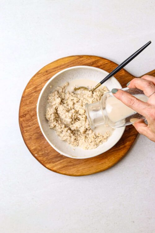 Creamy oatmeal being poured into a bowl with a spoon, served on a wooden tray for healthy breakfast.