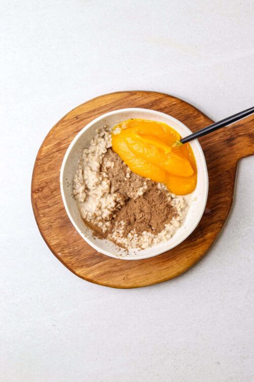 Creamy oatmeal with peaches and cinnamon in a white bowl on a wooden platter, healthy breakfast idea.