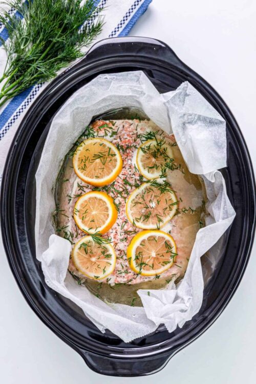 Tilapia fish in slow cooker with lemon slices and herbs, ready for baking, cooked with fresh dill and easy seafood recipe.