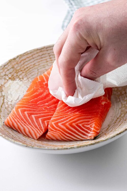 Fresh raw salmon fillets being cleaned with a paper towel.