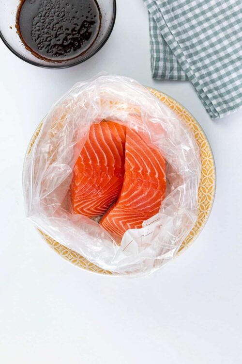 Fresh salmon fillet in vacuum-sealed bag on a decorative plate for baking or cooking.