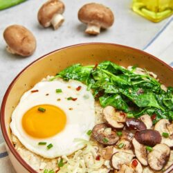 Savoury mushroom and spinach rice bowl with fried egg, cheese, and fresh green onions. Healthy, comforting breakfast or dinner option.