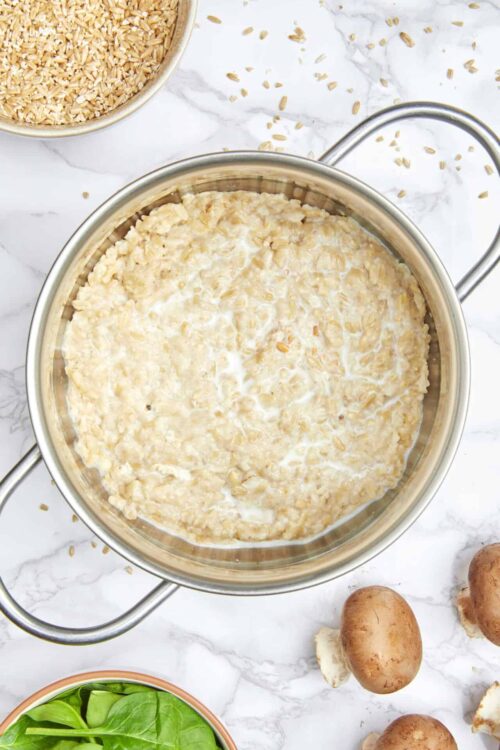 Creamy mushroom risotto cooking in a silver pot on marble countertop.