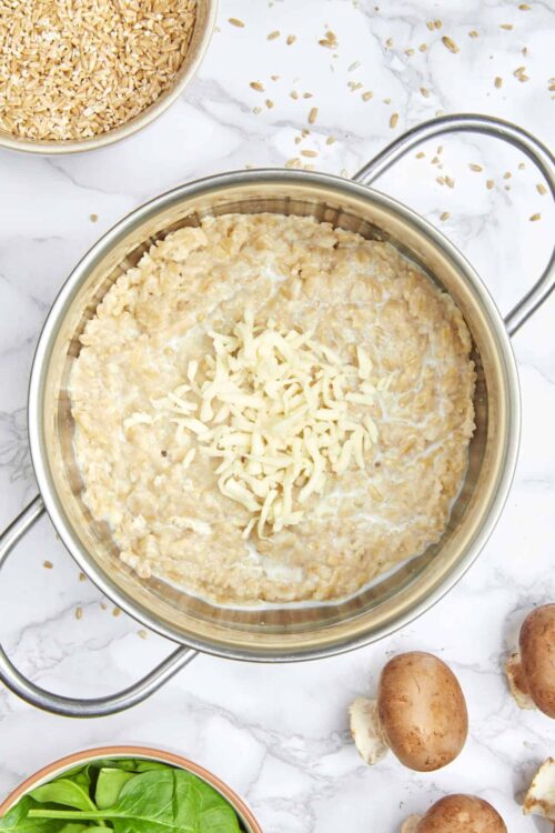 Creamy mushroom risotto cooking in a stainless steel pan with shredded cheese on top.