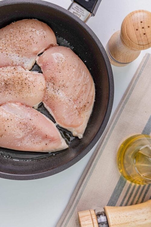 Juicy raw chicken breasts seasoned with salt and pepper in a black skillet.