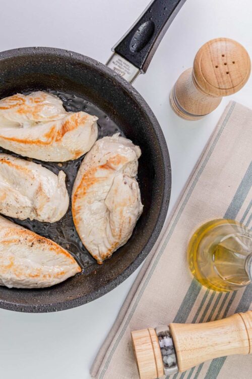 Juicy chicken breasts being cooked in a skillet on a stovetop.