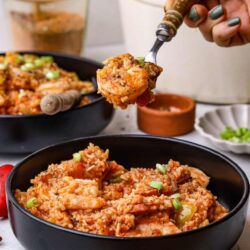 Savory shrimp and rice casserole with fresh green onions in a black bowl.