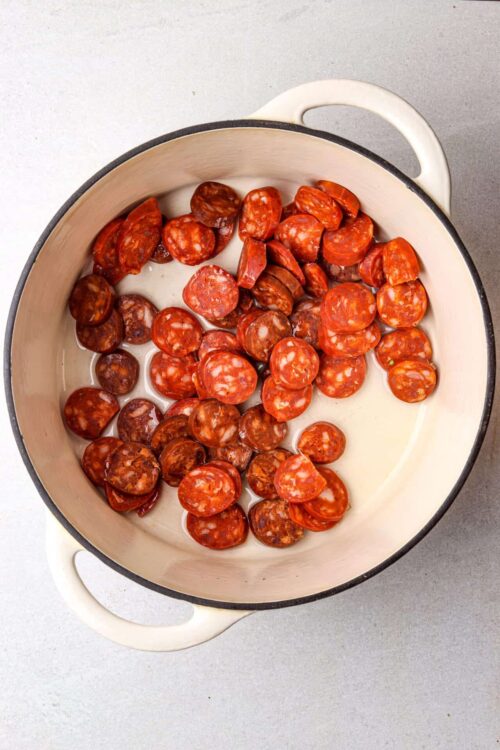 Spicy pepperoni slices in a white enamel skillet with cream sauce, ready for baking.