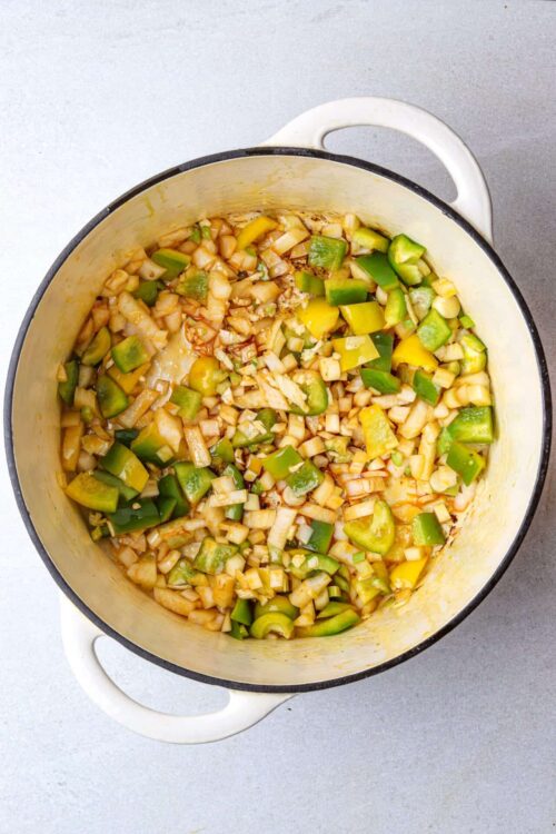 Chopped vegetables in a white enameled cast iron Dutch oven for hearty vegetable stew or soup.