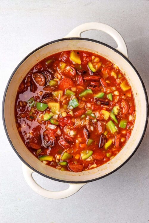 Savory vegetable chili in a white enamel-coated cast iron pot with tomatoes and beans.