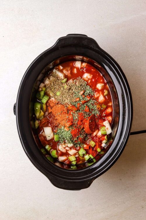 Seasoned vegetable and tomato soup in slow cooker with herbs and spices, ready to cook.