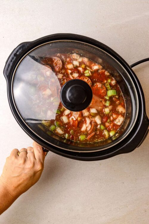 Slow cooker vegetable soup with tomatoes and herbs in a black crockpot.
