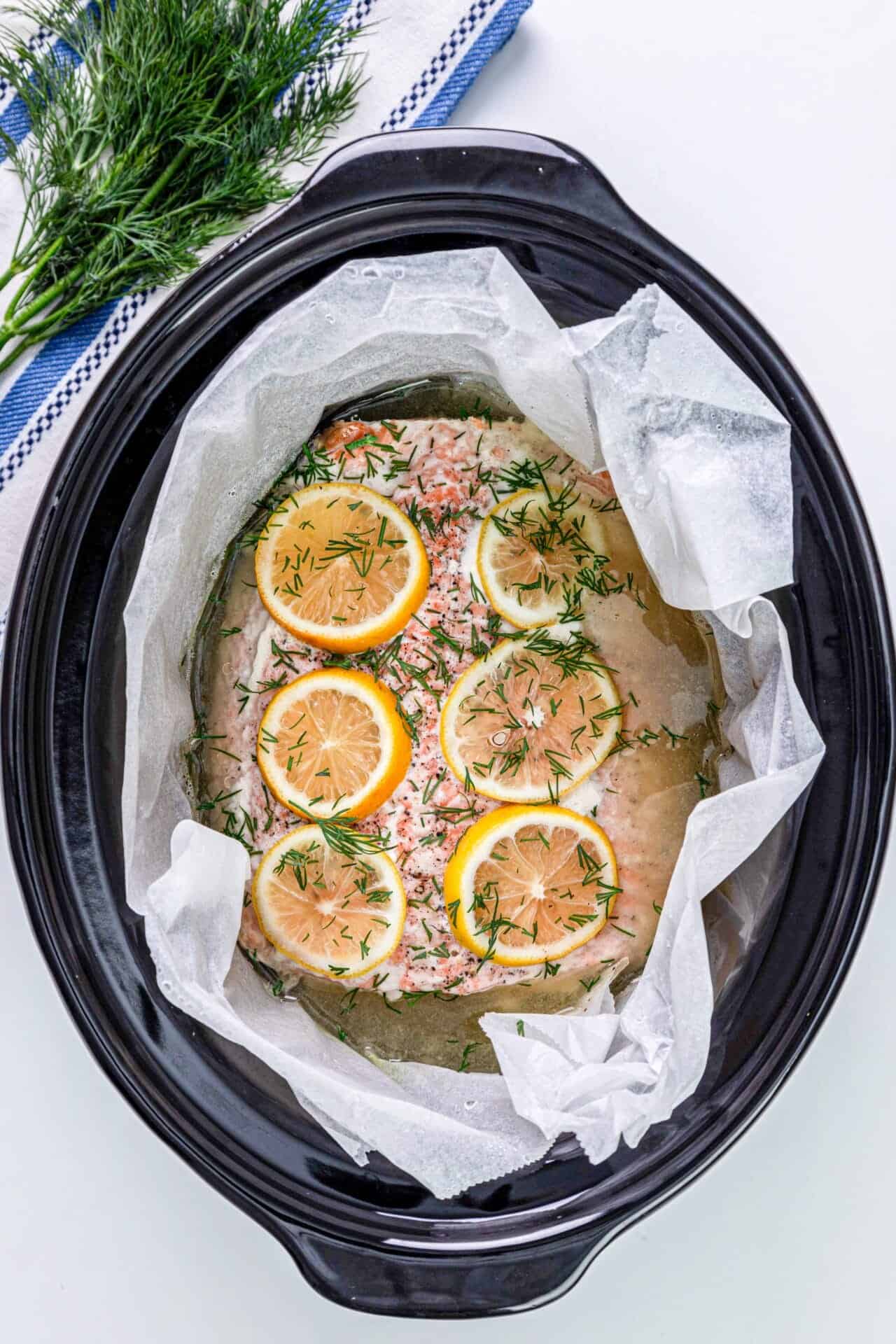 Baked salmon with lemon slices and fresh dill in a slow cooker, ready to cook.