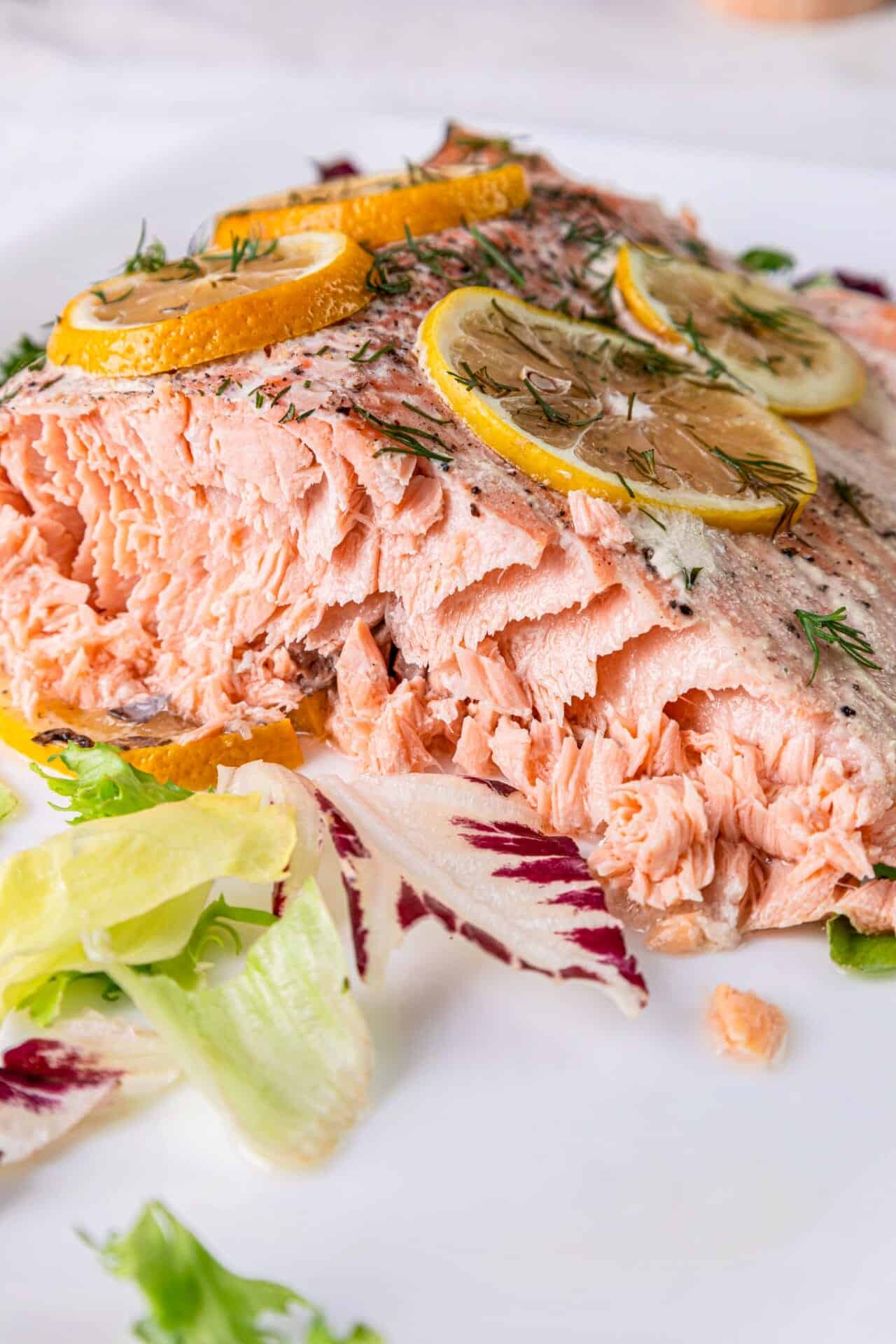 Fresh baked salmon fillet garnished with lemon slices, herbs, and a side salad, perfect for healthy seafood recipes.
