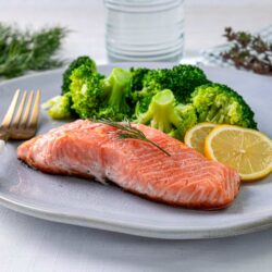 Fresh baked salmon with lemon slices and steamed broccoli on a white plate, healthy seafood dinner option.