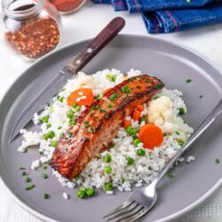 Succulent roasted salmon fillet on a bed of rice and vegetables, garnished with chopped chives for a healthy meal.
