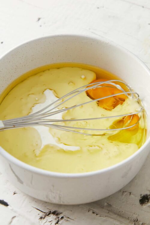 Creamy egg mixture with a whisk in a white bowl on a rustic surface.
