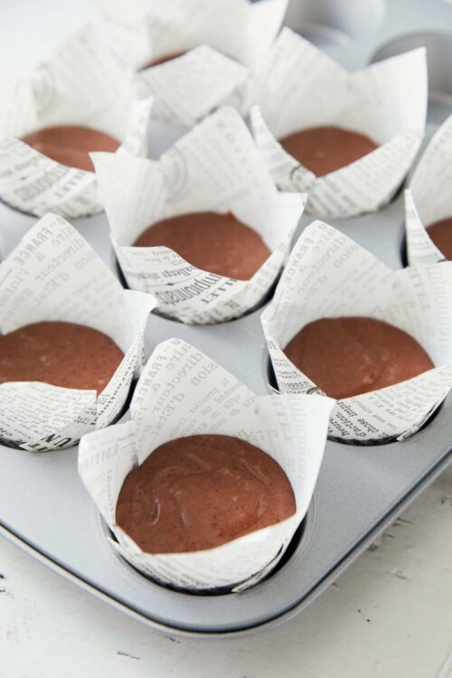 Freshly baked chocolate cupcakes in baking cups lined with newspaper-style parchment paper.