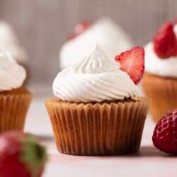 Delicious strawberry cupcakes with white frosting and fresh strawberry garnishes on a light pink background.