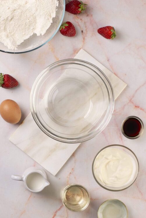 Flour, eggs, strawberries, vanilla, and dairy ingredients for baking strawberry shortcake.