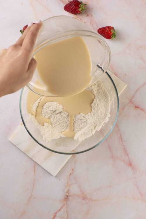Cream being poured into dry ingredients for baking between strawberries.