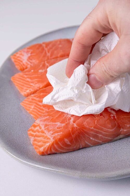 Fresh salmon fillets being wiped with a napkin for cooking or preparation.