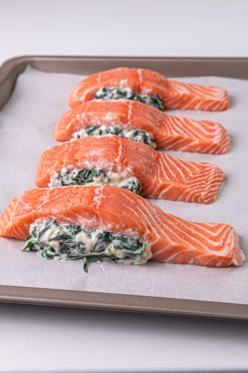 Fresh salmon fillets stuffed with spinach and cream cheese on baking sheet.