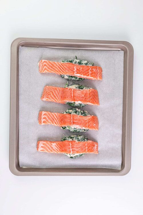 Fresh salmon fillets stuffed with spinach and cream cheese on a baking sheet.