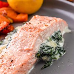 Juicy baked salmon fillet with creamy spinach sauce on gray plate.