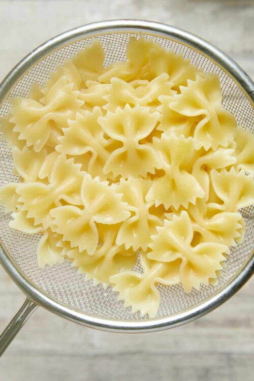 Fresh cooked bowtie farfalle pasta in a stainless steel sieve.