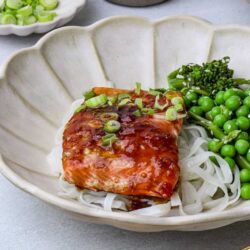 Fresh glazed salmon with green peas and spring onions in a white ceramic bowl.