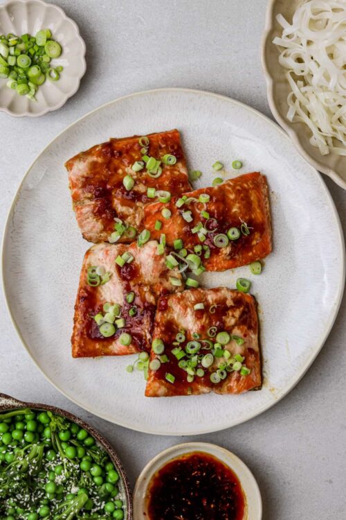 Sausage and green onion ham slices on white plate, Asian-inspired dish with soy sauce, noodles, and fresh vegetables.