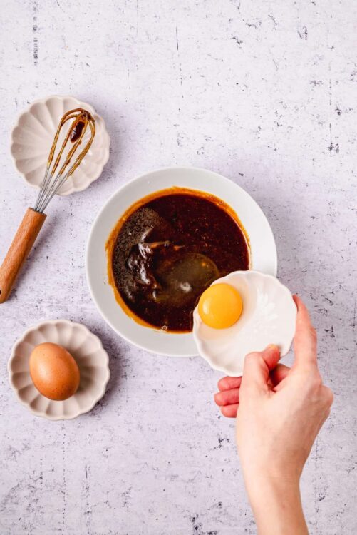 Rich brown gravy with an egg and baking ingredients on a white textured surface.