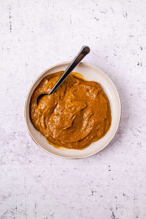 Creamy peanut butter spread in a white bowl on textured white background, perfect for sandwich recipes.
